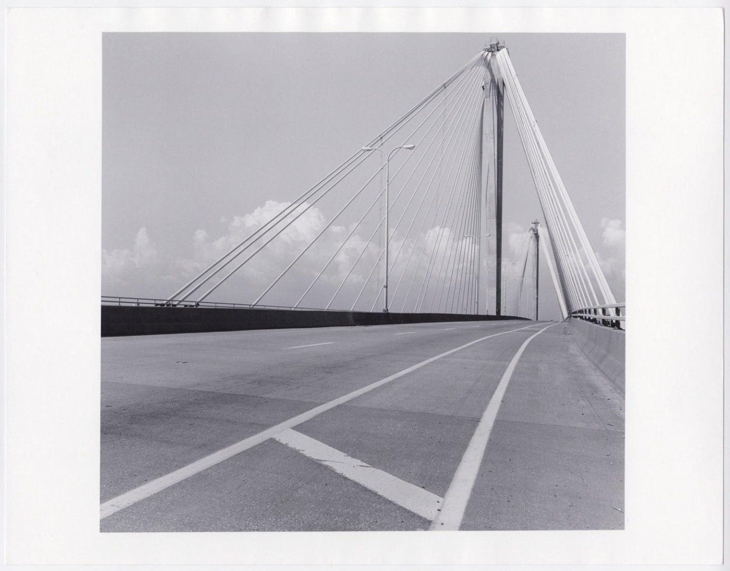 The Clark Bridge, a span of bridge moves across the bottom of the frame, turning slightly, arcing away. Above, only sky and suspension lines