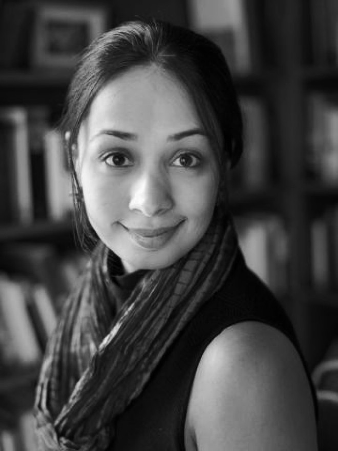 A portrait photo of Ayesha Ramachandran. In the background, blurred, bookshelves.